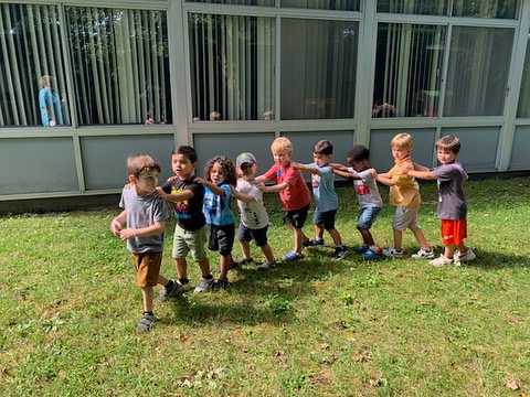Photo of a group of happy young children playing outside, linking themselves into a human chain with their arms